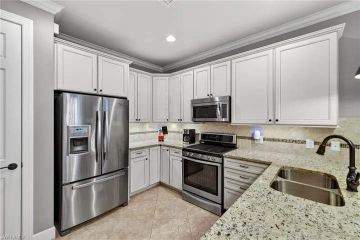 Kitchen featuring white shaker cabinetry, stainless steel appliances, speckled stone countertops, and a tile backsplash with decorative accents