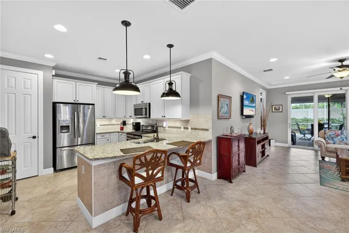 Open-concept kitchen and living area featuring tile flooring, white shaker cabinetry, stainless steel appliances, and an island with bar seating