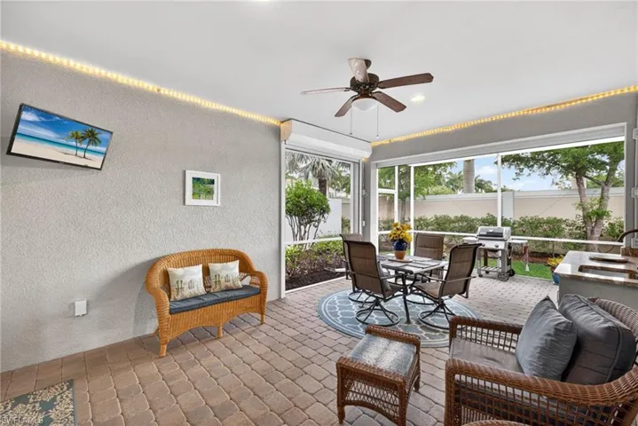 Screened patio featuring paver flooring, a ceiling fan with integrated lighting, and an outdoor kitchen area with built-in cabinetry and a countertop