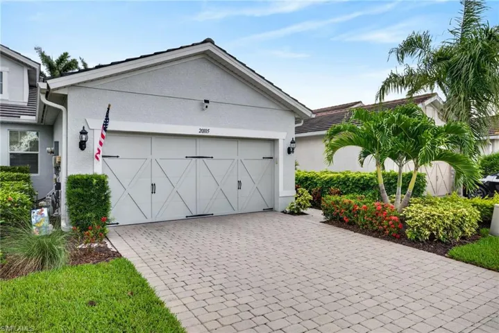 Front exterior featuring a decorative garage door, paver driveway, tropical landscaping, exterior lighting fixtures, and stucco siding