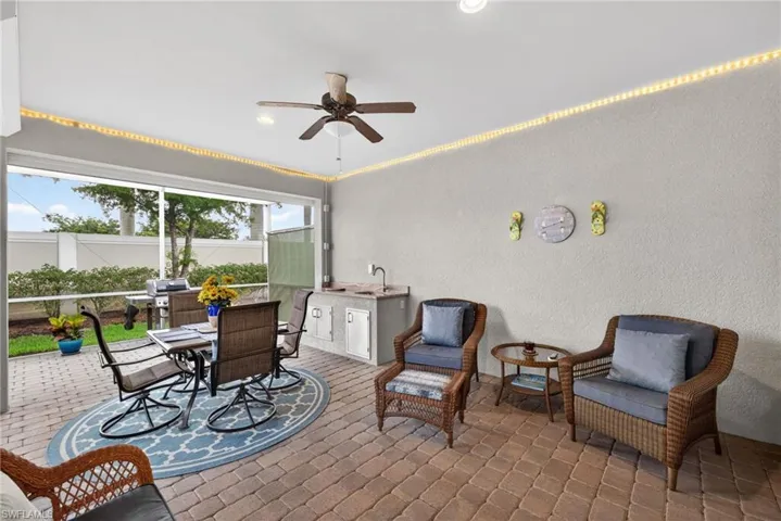 Screened-in outdoor living space featuring paver flooring, built-in outdoor kitchen with sink, ceiling fan, and recessed lighting