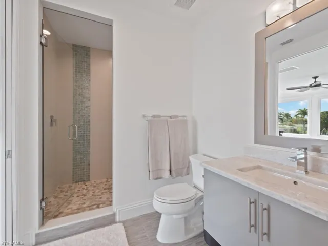 Bathroom featuring tile patterned floors, a shower with door, vanity, toilet, and ceiling fan