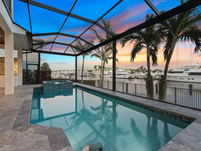 Pool at dusk featuring a lanai, a water view, a patio, and an in ground hot tub
