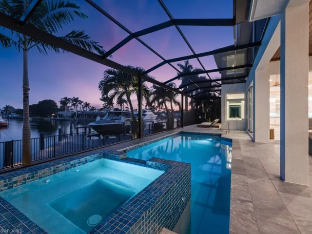 Pool at dusk featuring an in ground hot tub, a lanai, a water view, and a patio