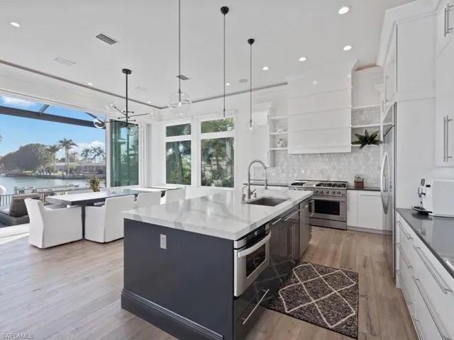 Kitchen featuring white cabinetry, appliances with stainless steel finishes, decorative light fixtures, a water view, and sink