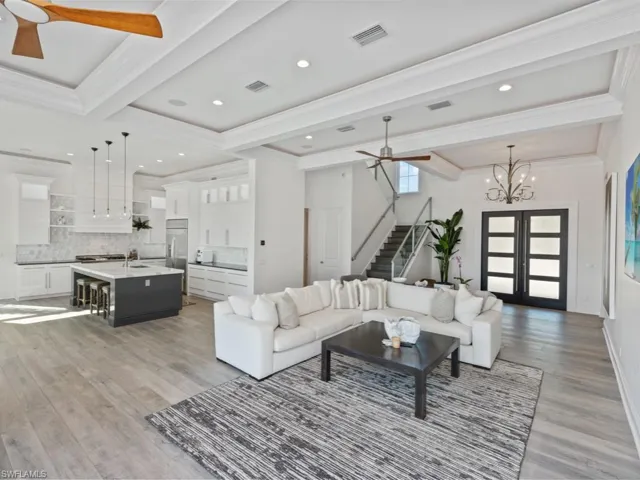 Living room with french doors, ceiling fan with notable chandelier, ornamental molding, and light hardwood / wood-style flooring