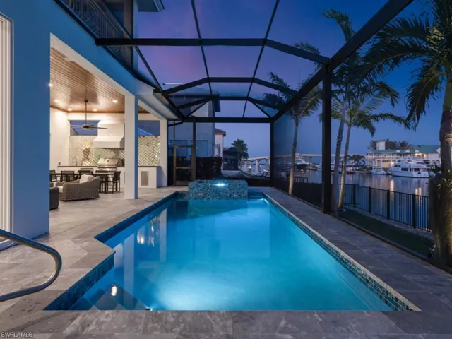 Pool at twilight featuring a patio area, outdoor lounge area, an in ground hot tub, glass enclosure, and a water view