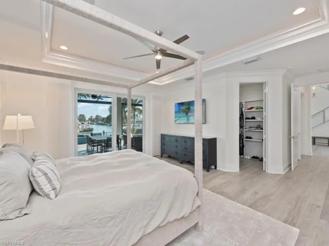 Bedroom featuring ceiling fan, light hardwood / wood-style floors, access to outside, a raised ceiling, and a walk in closet