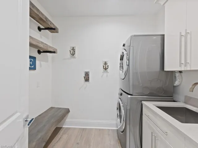 Clothes washing area featuring cabinets, sink, stacked washer and dryer, and light wood-type flooring