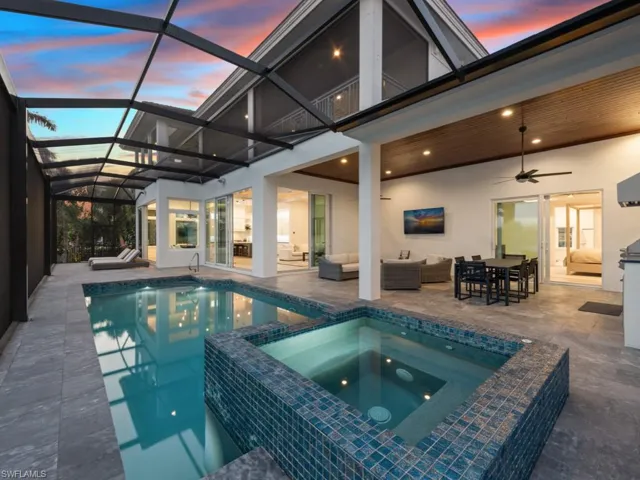 Pool at dusk with glass enclosure, ceiling fan, an outdoor hangout area, an in ground hot tub, and a patio