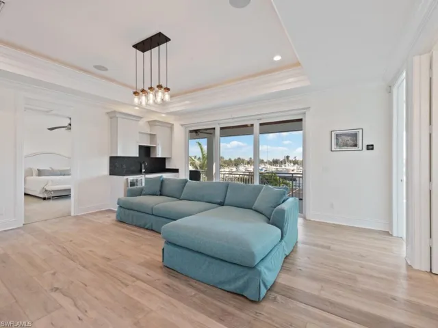 Living room with ceiling fan with notable chandelier, sink, ornamental molding, a raised ceiling, and light hardwood / wood-style flooring
