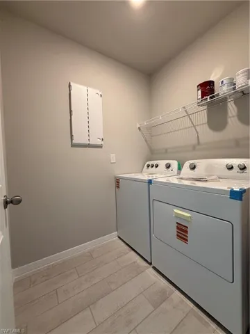 Laundry area with electric panel, separate washer and dryer, light wood finished floors, and baseboards