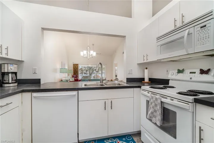 Kitchen featuring white cabinetry, white appliances, and window to dining area