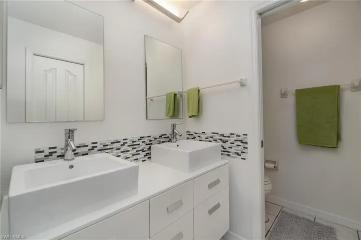 Primary Bathroom featuring tile flooring, decorative backsplash, and modern dual sinks