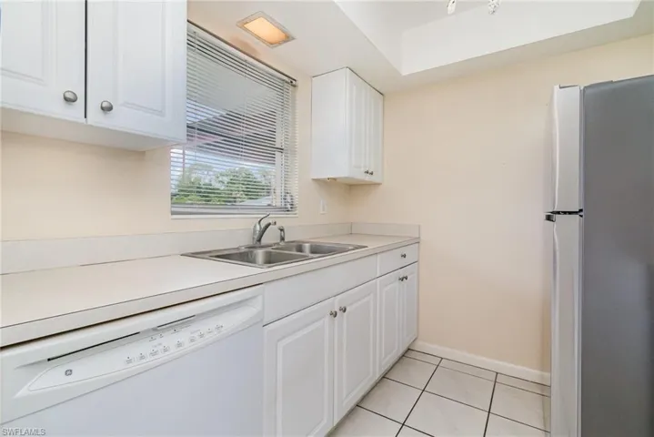 Kitchen with freestanding refrigerator, white cabinetry, white dishwasher, and light countertops