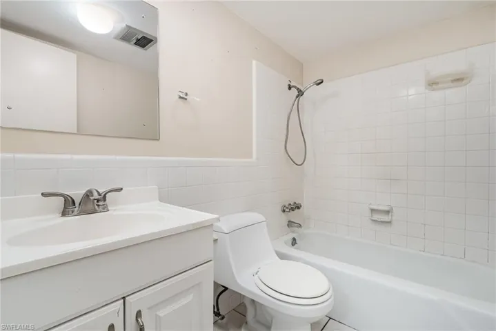 Bathroom with vanity, tile walls, washtub / shower combination, and a wainscoted wall