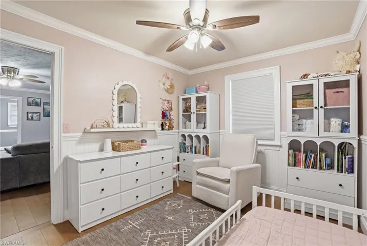 Room featuring wood-finish flooring, crown molding, a ceiling fan, and window with blinds