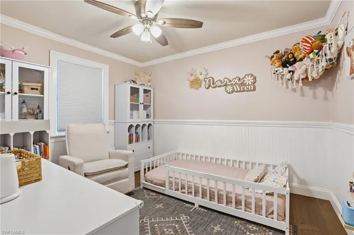 Room featuring beadboard wainscoting, crown molding, a window with blinds, wood-finish flooring, and a ceiling fan with integrated lighting