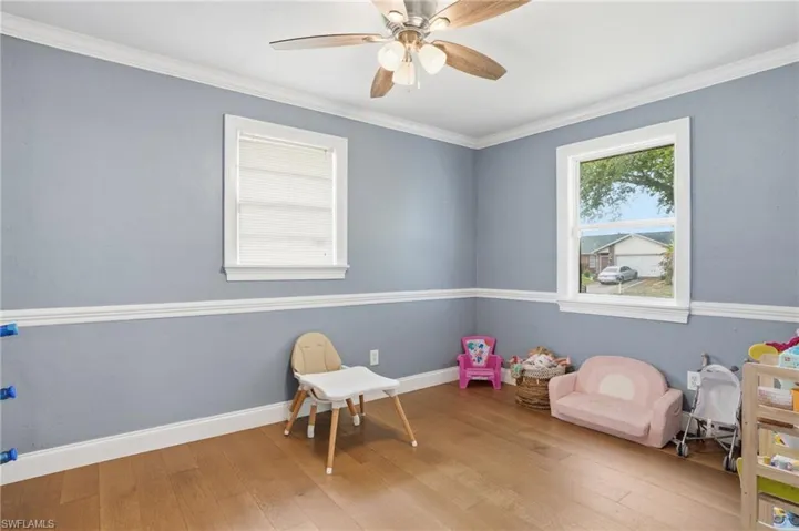 Room featuring wood-finish flooring, two windows, crown molding, and a ceiling fan with integrated lighting
