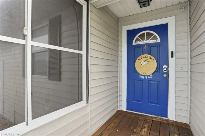 Entryway featuring a vibrant blue door with a sunburst transom window, white trim, and a wood-finish porch floor