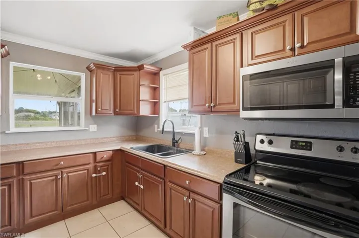 Kitchen featuring warm wood cabinetry, light-toned countertops, and a stainless steel appliance suite including an over-the-range microwave and electric stove