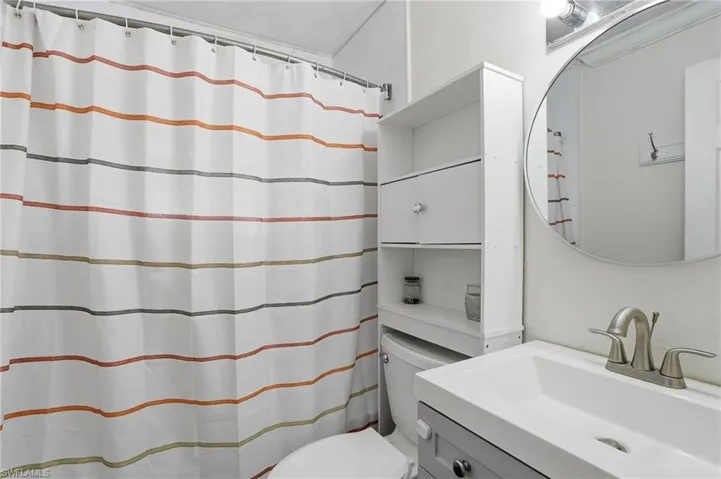 Bathroom featuring a white vanity with a rectangular sink, brushed nickel faucet, and a round mirror
