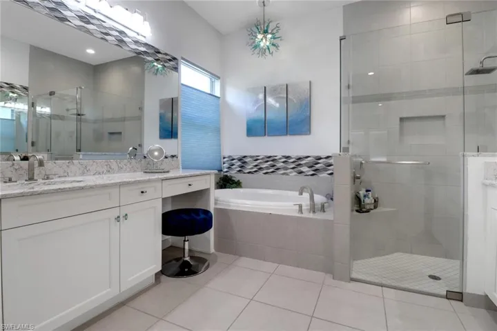 Primary bath featuring dual vanities with two sinks, a relaxing soaking tub, and a separate shower. Enhanced by a beautiful chandelier-style light fixture.