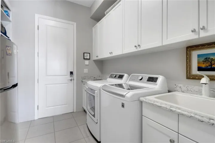 Thoughtfully designed laundry space with custom shelving, laundry tub, secondary fridge, and wine cooler for added convenience