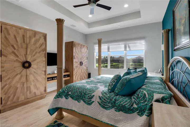 Spacious primary bedroom with tray ceiling, ceiling fan, and peaceful lake views