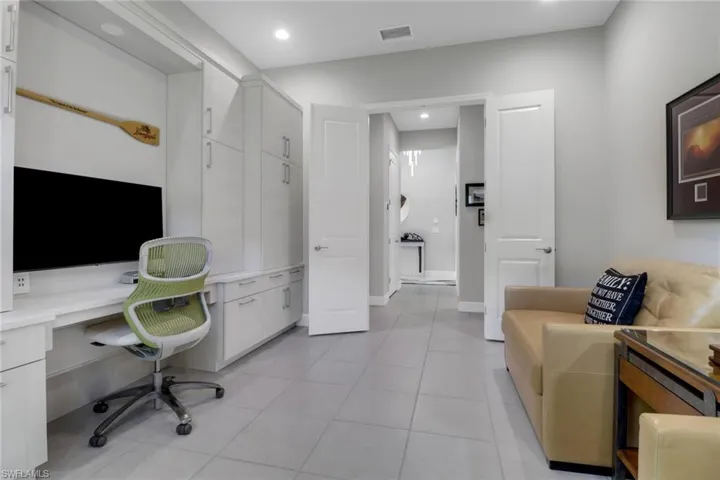 Spacious den featuring a full wall of custom cabinetry, built-in desk, large window with natural light, and ceiling fan—perfect for a home office or media room.