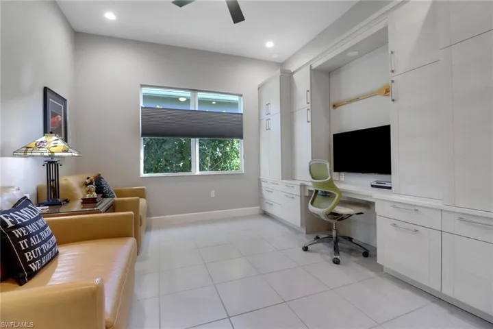 Spacious den featuring a full wall of custom cabinetry, built-in desk, large window with natural light, and ceiling fan—perfect for a home office or media room.