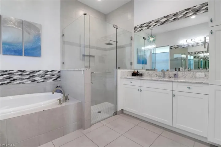 Primary bath featuring dual vanities with two sinks, a relaxing soaking tub, and a separate shower. Enhanced by a beautiful chandelier-style light fixture.