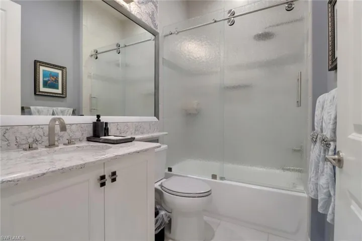 Inviting guest bathroom boasts a decorative framed mirror and a tub with an upgraded sliding shower door for convenience