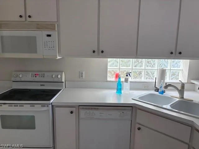 Kitchen featuring white appliances, light countertops, and white cabinets
