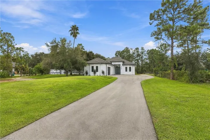 Single-story exterior featuring white stucco siding, a multi-gabled roof, expansive manicured lawn, and a paved concrete driveway