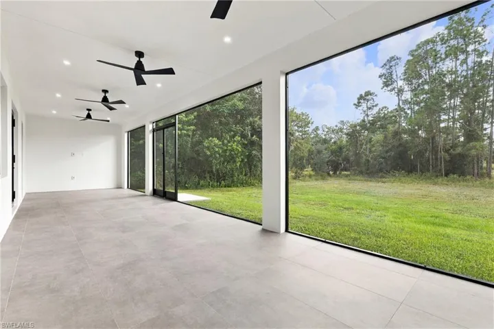 Rear exterior featuring a covered lanai with screen enclosure, tile roof, and expansive lawn