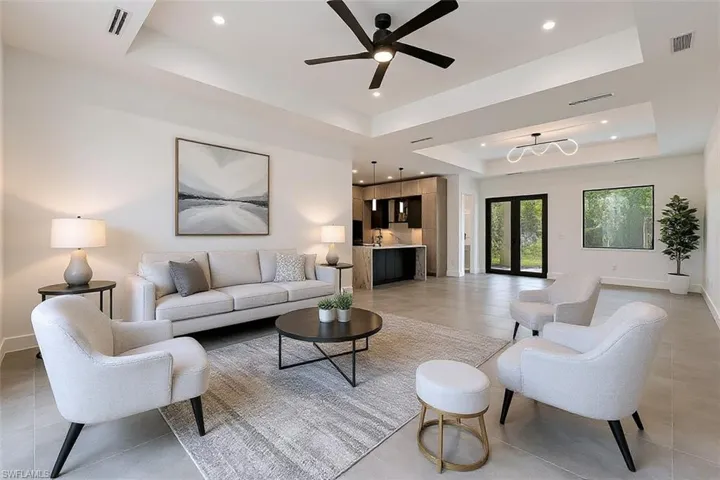 Tray ceilings with recessed lighting, large-format tile flooring, a modern matte black ceiling fan, and linear pendant lighting above a kitchen island with dark cabinetry