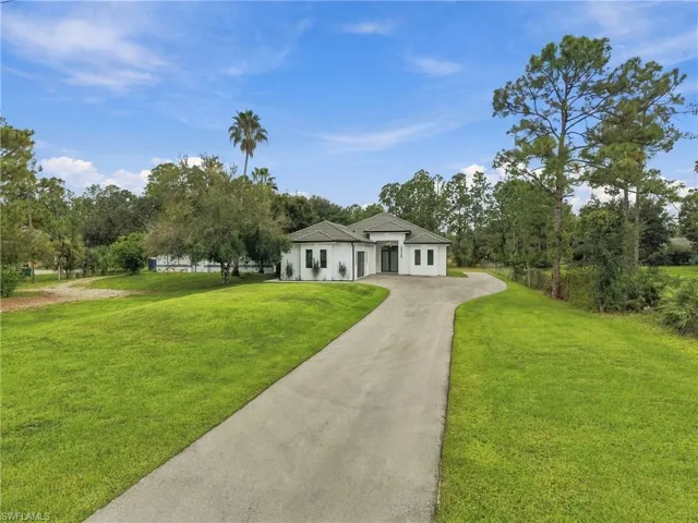 Aerial view of a residential property featuring a sprawling lot, expansive green space, paved driveway, and mature woodland surroundings