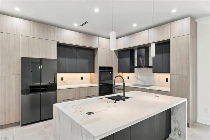 Modern kitchen featuring wood-finish cabinetry, matte black upper cabinets, stone-surfaced countertops, a full-height stone backsplash, and a center island with an integrated workstation sink