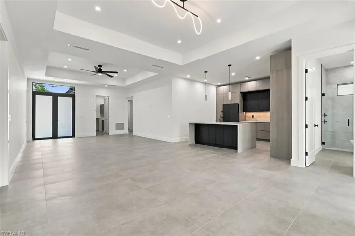 Modern kitchen featuring a central island with a stone-finish waterfall edge, two-tone cabinetry, recessed lighting, tile flooring, and a tray ceiling with a contemporary light fixture