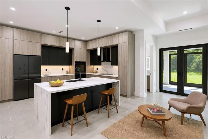 Kitchen featuring floor-to-ceiling cabinetry, a central island with a waterfall countertop, integrated wall ovens, and matte black fixtures