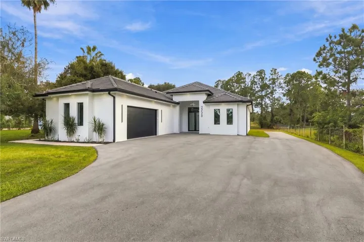 Single-story residence featuring a smooth stucco exterior, dark-toned tile roof, expansive asphalt driveway, and a two-car garage with a solid-panel door