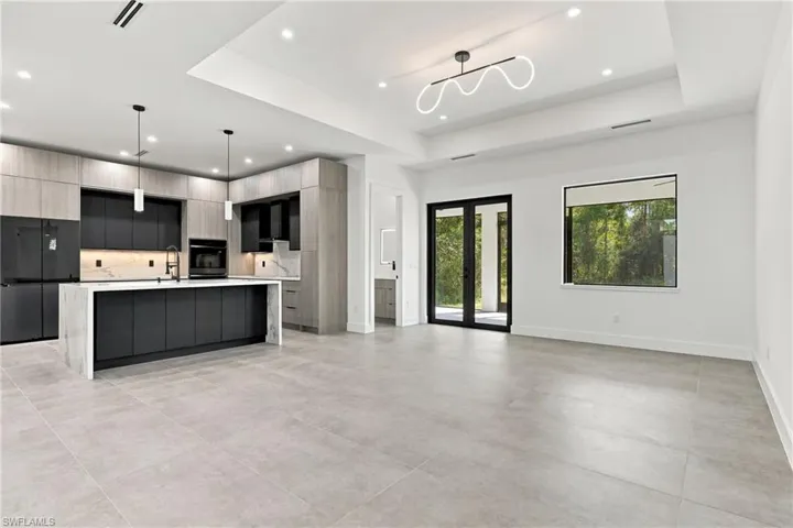 Modern kitchen featuring a waterfall-edge island, two-tone cabinetry with wood-finish and matte black finishes, stone-look backsplash and countertops, and glass-paneled exterior double doors