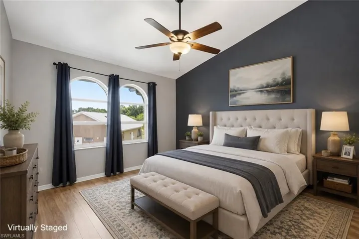 Vaulted ceiling with a ceiling fan, two arched windows, wood-finish flooring, and a contrasting accent wall