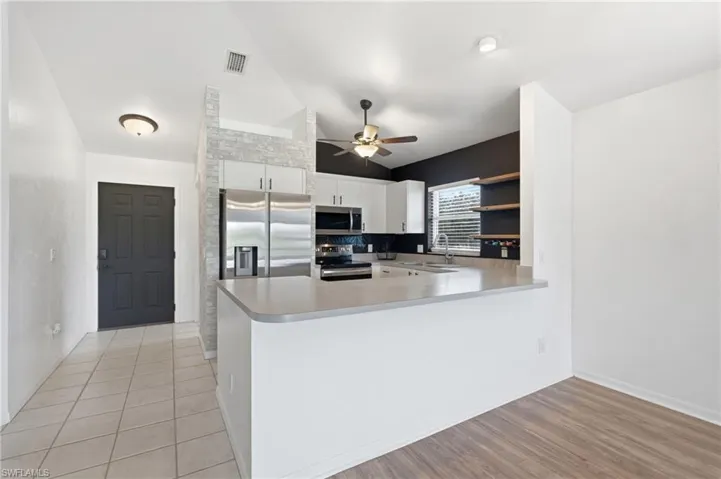 Open-concept kitchen with stainless steel appliances, white cabinetry, integrated sink, and light-toned countertops