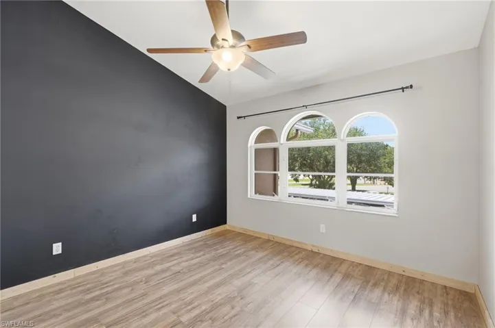 Vaulted ceiling with a ceiling fan, three arched windows, wood-finish flooring, and a contrasting accent wall