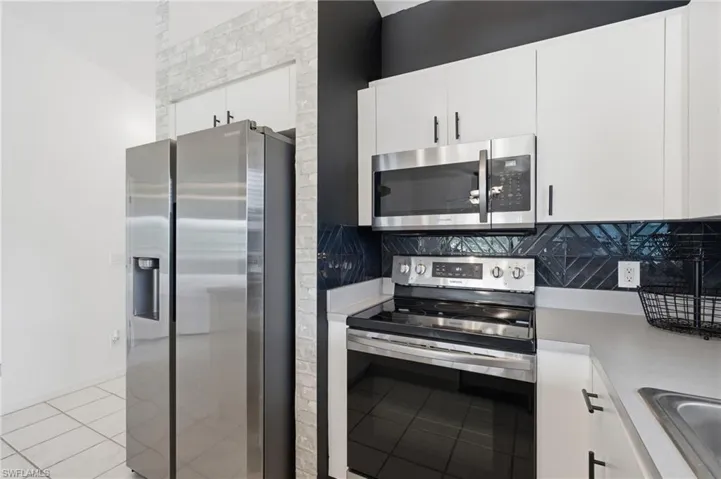 Stainless steel appliances, white cabinetry, dark herringbone tile backsplash, light countertop, and tile flooring
