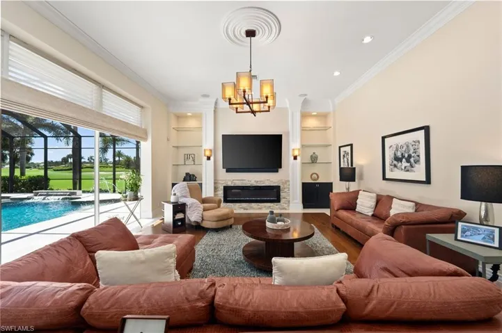 Living area with built in features, ornamental molding, wood finished floors, a glass covered fireplace, and recessed lighting