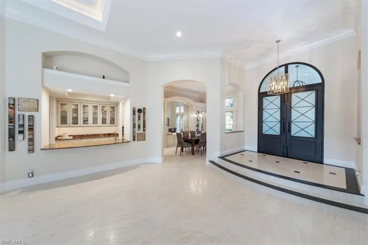 Foyer entrance with ornamental molding, a chandelier, a towering ceiling, french doors, and arched walkways