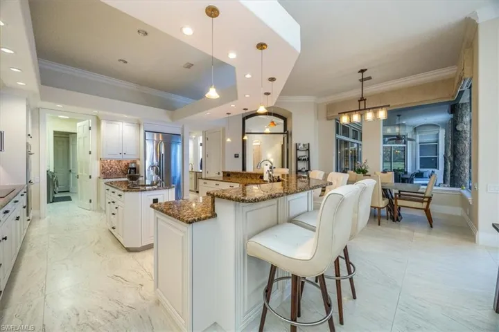 Kitchen with crown molding, a kitchen breakfast bar, pendant lighting, white cabinets, and a raised ceiling
